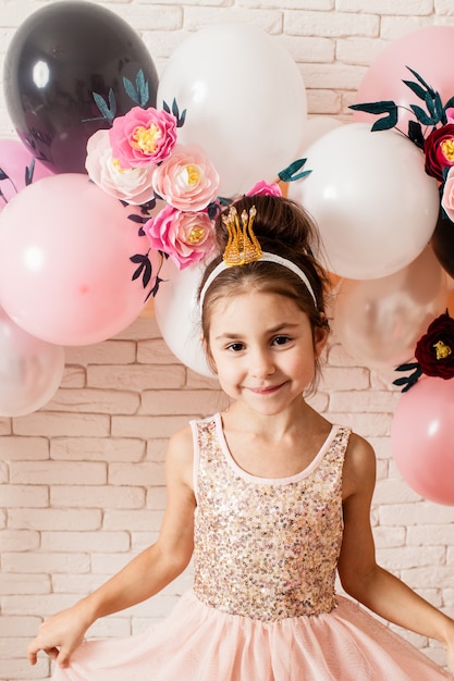 Das schöne kleine Mädchen mit Krone über rosa girly Ballon- und Papierblumendekorationen. Kleine Prinzessin feiert