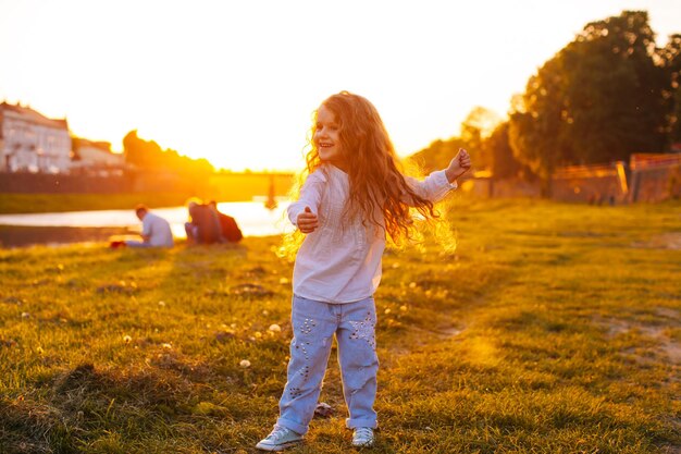 Das schöne kleine Mädchen tanzt bei Sonnenuntergang am Fluss Walzer