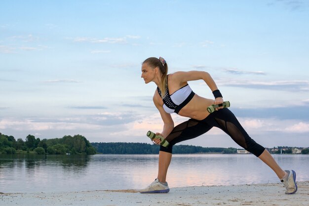 Foto das schöne mädchen mit einer sportfigur praktiziert yoga im freien in der nähe des sees. sommer.