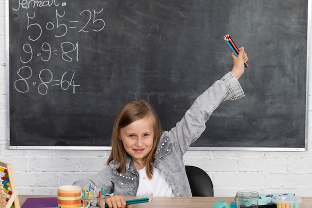 Das Schulmädchen sitzt höflich am Schreibtisch und eine Schultafel hängt hinten