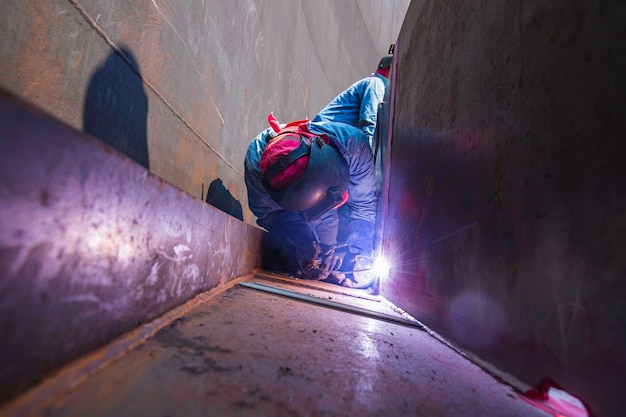 Das Schweißen von Metall durch männliche Arbeiter ist Teil des Baus von Maschinen, Tankdüsen, Rohrleitungen, Erdöl- und Gaslagertanks in geschlossenen Räumen