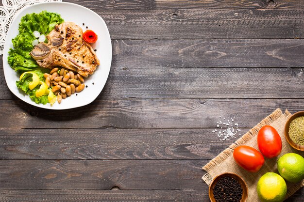 Das selbst gemachte Kochen des Schweinefleischsteaks mit Gewürzen verlässt Kopfsalat auf hölzernem Schneidebrett und einem Teller