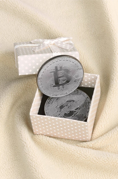 Das silberne bitcoin liegt in einer kleinen orangefarbenen geschenkbox mit kleiner schleife