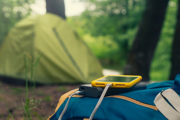 Das Smartphone wird mit einem tragbaren Ladegerät aufgeladen. Power Bank lädt das Telefon im Freien mit einem Rucksack vor der Kulisse eines Zeltes auf.