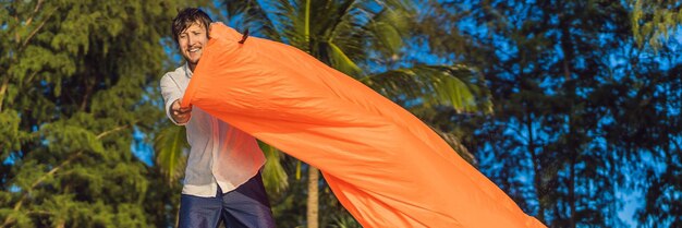 Das sommerliche Lifestyle-Porträt des Menschen bläst ein aufblasbares orangefarbenes Sofa am Strand der tropischen Insel auf