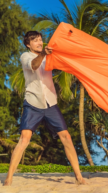 Das sommerliche Lifestyle-Porträt des Menschen bläst ein aufblasbares orangefarbenes Sofa am Strand der tropischen Insel auf