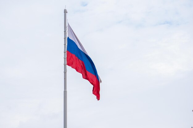 Das Staatssymbol der Russischen Föderation im Wind Eine große russische Flagge vor blauem Himmel mit Wolken in Nahaufnahme