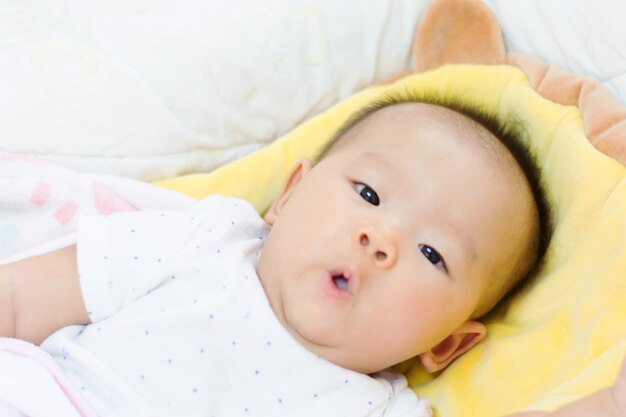 Das süße asiatische Baby, das auf Bett lag, wachte gerade auf