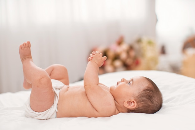 Das süße baby liegt auf dem rücken auf dem bett und spielt mit seinen händen