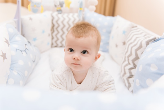 Das süße Baby liegt in einem weißen runden Bett. Leichter Kindergarten für kleine Kinder.