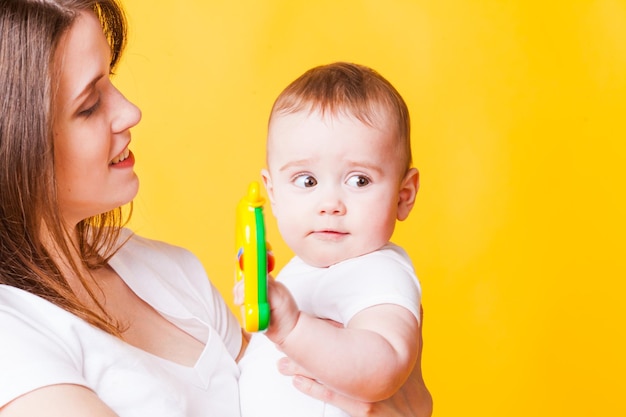 Das süße Baby mit einem Spielzeug an den Händen in der Mama, die neugierig zur Seite schaut