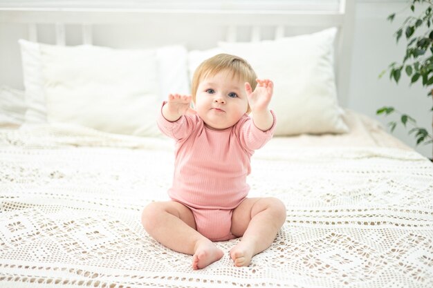 Das süße Babymädchen sitzt auf einem Bett mit weißer Bettwäsche im Schlafzimmer des Hauses. Ein Kinderporträt, das das Kind in die Kamera schaut