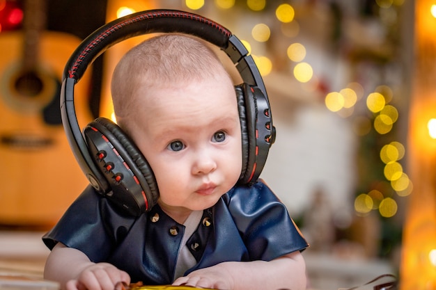 Das süße kleine Baby liegt mit Kopfhörern auf seinem Bauch und hört Musik.