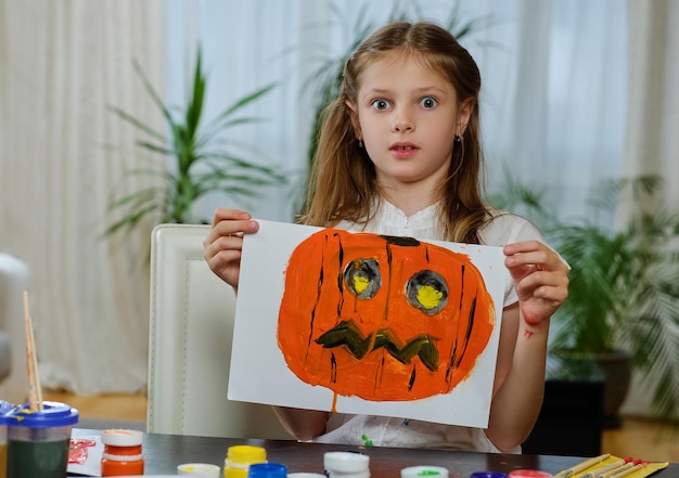 Das süße kleine Mädchen hält ein Poster mit bemaltem Halloween-Kürbis.