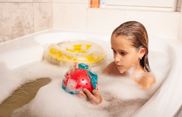 Das süße Mädchen badet in einem Schaumbad und spielt mit Spielzeugen, die sich das Meer vorstellen