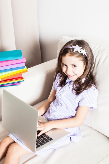 Das süße Mädchen hatte eine Idee. Das kleine Mädchen sitzt auf dem Sofa mit Laptop und Büchern