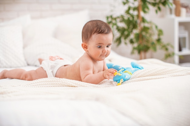 Das süße mollige Baby liegt auf dem Bauch und schaut sich das Spielzeug an.