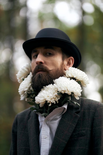 Das surreale Thema ein bärtiger Mann in Blazer und Hut mit einem Strauß weißer Blumen um den Hals