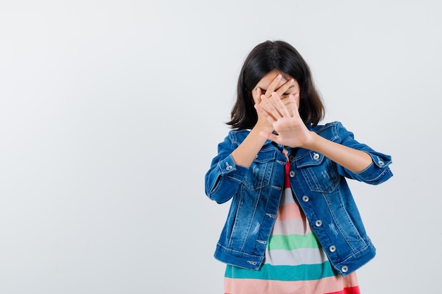 Das Teenager-Mädchen bedeckt sein Gesicht mit der Hand und zeigt mit anderen auf weißem Hintergrund eine Stopp-Geste