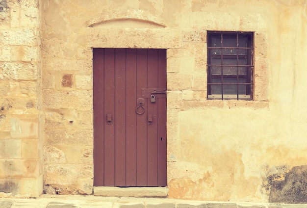 Das Texturmuster Die alte beige Hintergrundwand aus Naturstein mit Tür und Fenster