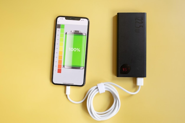 Das tragbare Ladegerät lädt ein Smartphone isoliert auf gelbem Hintergrund auf. Powerbank