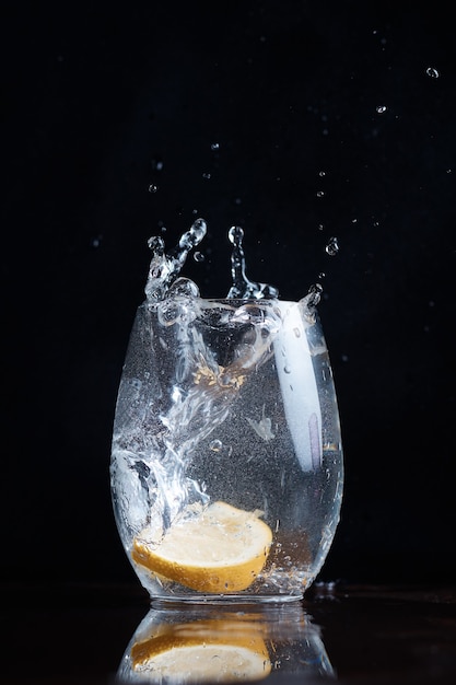 Das Trinken von kohlensäurehaltigem Wasser lässt Zitronen-Zitrusfrüchte in ein klares Glas fallen und spritzt verschwommen