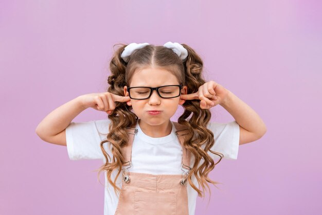 Das verärgerte Mädchen steckte sich die Finger in die Ohren. Baby auf einem lila isolierten Hintergrund.