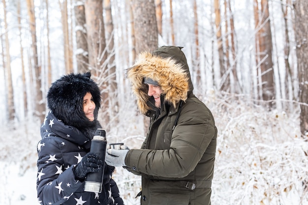 Das verliebte junge Paar trinkt ein heißes Getränk aus einer Thermoskanne und genießt die Winternatur.