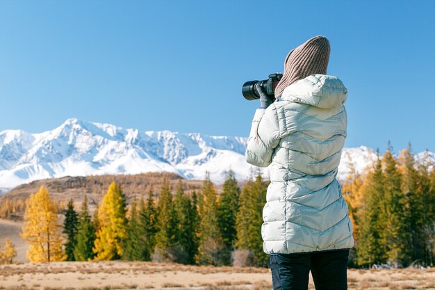 Das Wandern der jungen Frau macht Fotos auf einer Gebirgskamera. Frauenblogger, der Foto durch Kamera von Schneespitzenbergen macht.