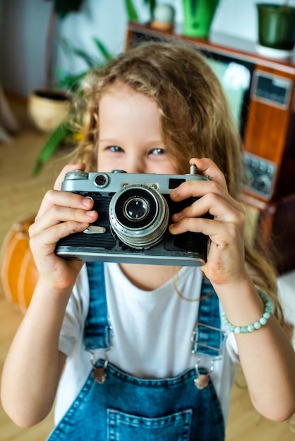 Das weiße Teenager-Mädchen fotografiert mit einer Retro-Kamera und lacht Hobby für Kinder und eine glückliche Kindheit