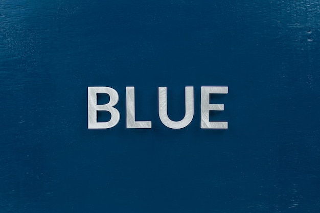Das Wort Blau mit silbernen Metallbuchstaben auf klassischem blau bemaltem Bretthintergrund