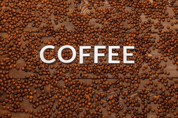 Das Wort Kaffee mit silbernen Buchstaben auf Kaffeebohnen aus Holzbrettoberfläche gelegt