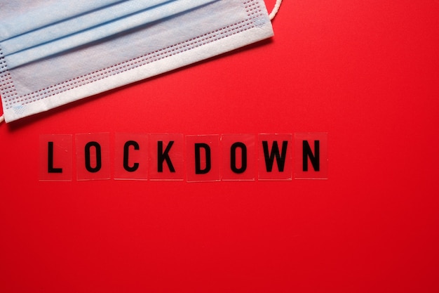 Das Wort Lockdown und eine medizinische Maske auf einem roten Hintergrund. Zweite Welle covid 19.
