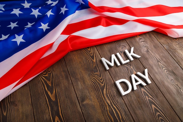 Das Wort MLK-Tag mit silbernen Metallbuchstaben auf Holzoberfläche mit zerknitterter US-Flagge gelegt