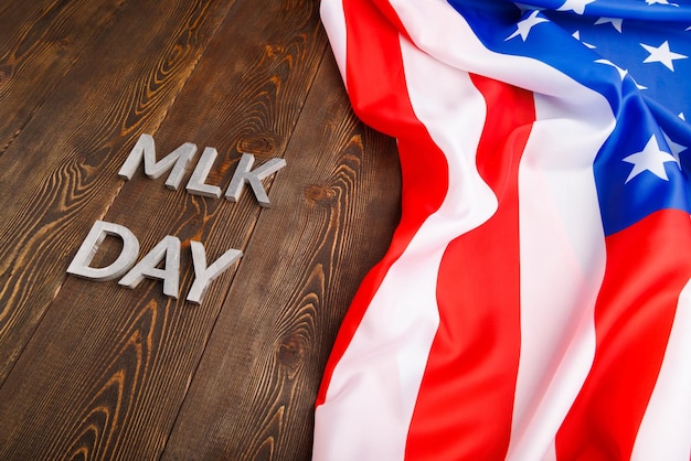 Das Wort MLK-Tag mit silbernen Metallbuchstaben auf Holzoberfläche mit zerknitterter USA-Flagge an der Oberseite