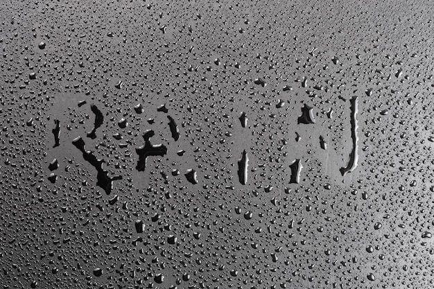 Foto das wort regen handgeschrieben auf matte schwarze hydrophobe matte oberfläche mit wassertropfen