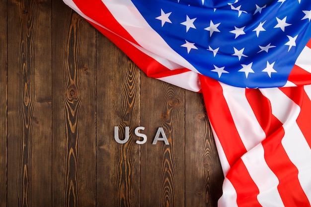 Das Wort USA mit silbernen Metallbuchstaben auf Holzbrettoberfläche unter zerknitterter Flagge der Vereinigten Staaten von Amerika gelegt