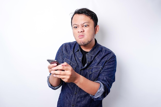 Das wütende und wütende Gesicht des asiatischen Mannes im blauen Hemd, das sein Telefon hält, isolierte weißen Hintergrund