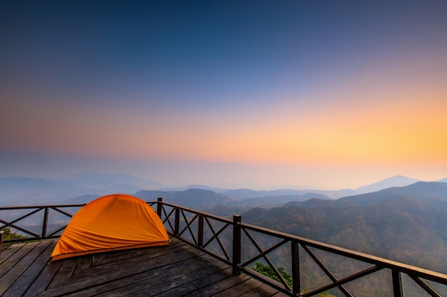 Das Zelt des orange Wanderers auf der hölzernen Terrasse im hohen Berg.