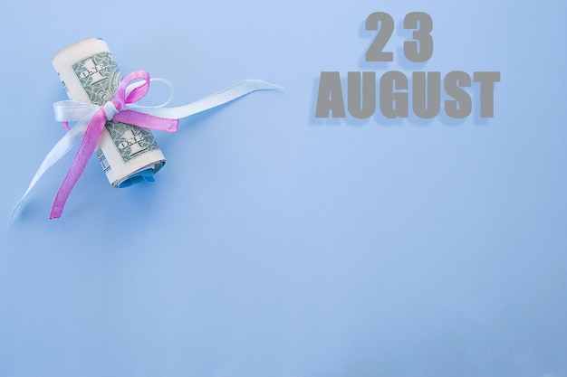 Data do calendário em fundo azul com notas de dólar enroladas fixadas pela fita rosa azul 23 de agosto