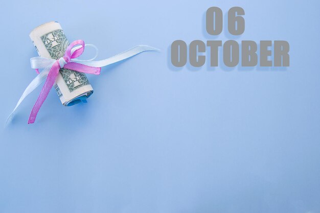 Data do calendário em fundo azul com notas de dólar enroladas fixadas por fita azul e rosa com espaço de cópia 6 de outubro é o sexto dia do mês