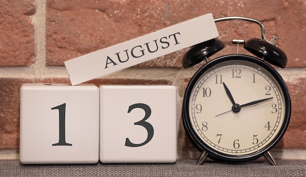 Data importante, 13 de agosto, temporada de verão. Calendário feito de madeira em um fundo de uma parede de tijolos. Despertador retro como um conceito de gerenciamento de tempo.