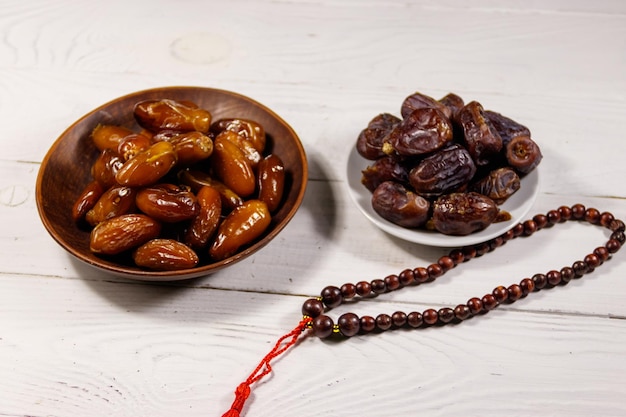 Dátiles fruta y rosario en mesa de madera blanca