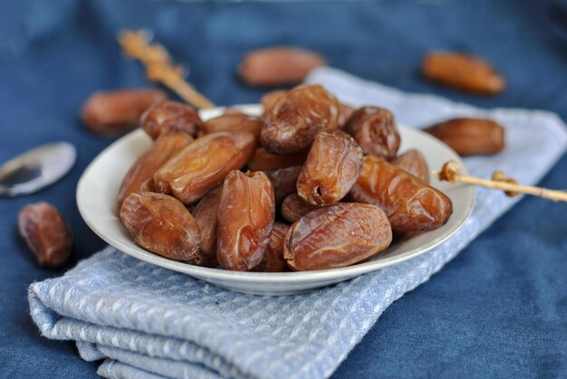 Dátiles maduros en un recipiente blanco en la superficie azul Tiempo de Ramadán