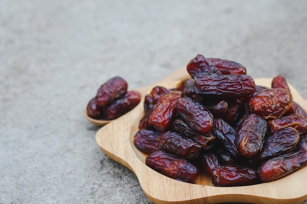 Los dátiles en un plato de madera sobre un suelo de cemento son frutos secos marrones que se pueden comer enteros