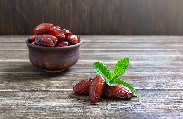 Dátiles secados al sol y hojas de menta fresca en un cuenco de cerámica sobre una mesa de madera. Frutos secos orgánicos.