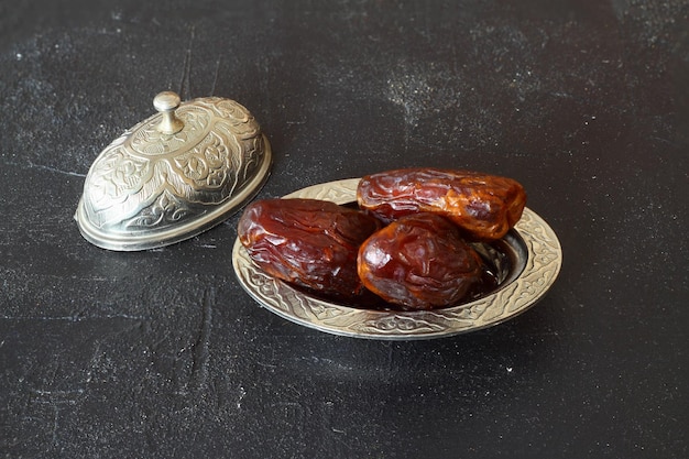 Dátiles secos en una mesa de madera en primer plano de platos de plata Composición de dátiles secos en un plato de ramadán