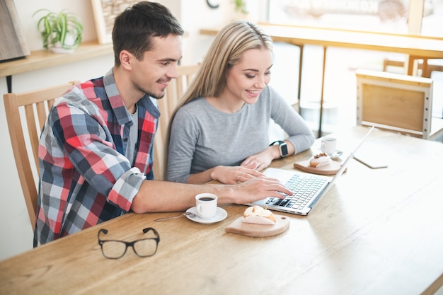 Datum im Café. Junges Paar im Café mit stilvollem Interieur. Studenten mit leckeren Kaffeegetränken. Sie chatten, benutzen Laptop und lächeln