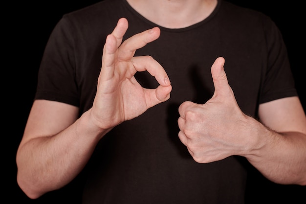 Daumen hoch und OK signalisieren Mannhandgeste. Daumen hoch OK-Zeichen, schwarzer Hintergrund. Positives Zeichen für Erfolg oder Zustimmung.