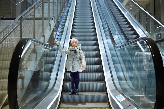 De baixo tiro da garota em pé na escada em movimento no terminal